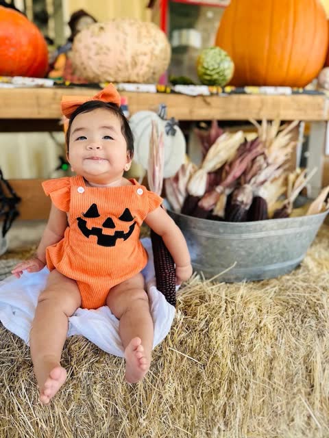 A baby in a pumpkin costume sits among gourds and decorative pumpkins
